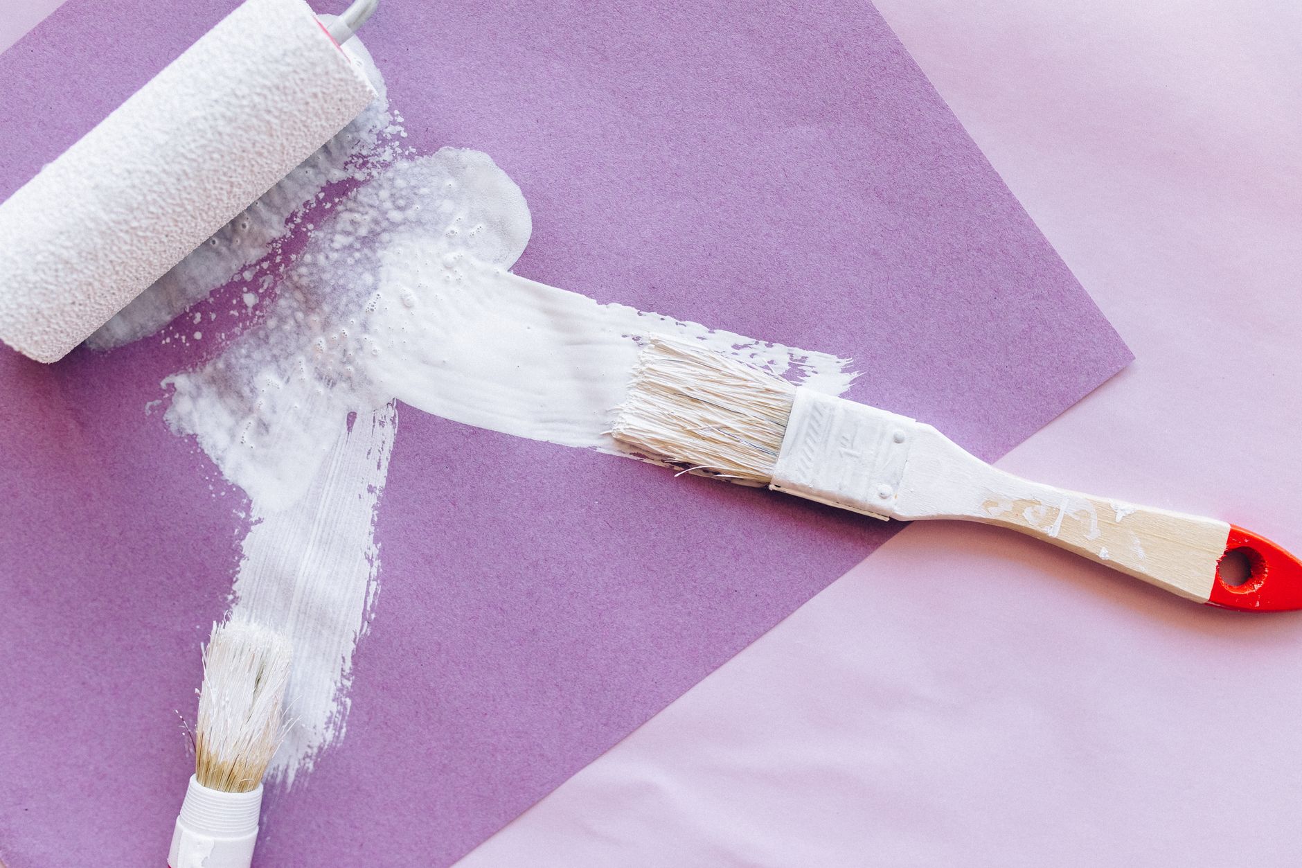 Overhead shot of paint brushes and roller applying white paint on purple paper with ample copy space in Temecula, CA